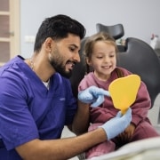 Happy cute little girl enjoying her beautiful toothy smile looking at mirror