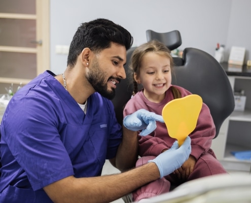 Happy cute little girl enjoying her beautiful toothy smile looking at mirror