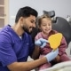 Happy cute little girl enjoying her beautiful toothy smile looking at mirror